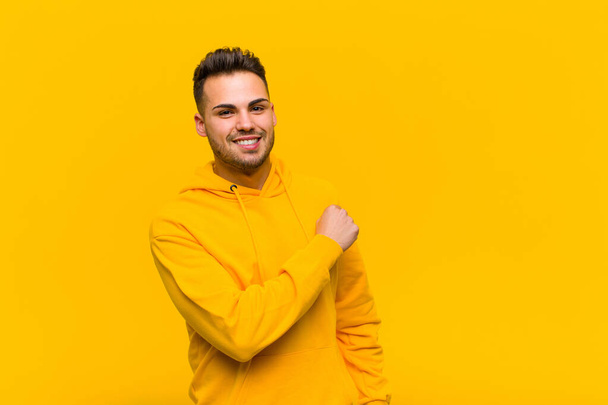young hispanic man feeling happy, positive and successful, motivated when facing a challenge or celebrating good results against orange wall - Fotoğraf, Görsel
