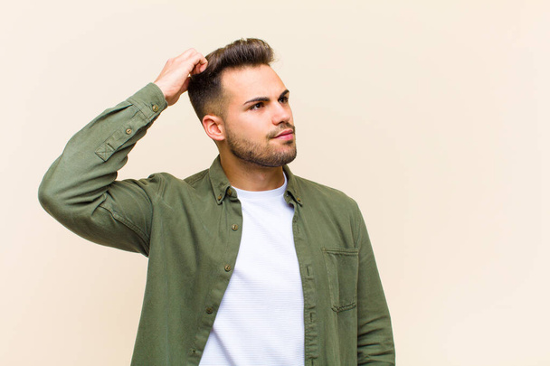 young hispanic man feeling puzzled and confused, scratching head and looking to the side against isolated background - Photo, image