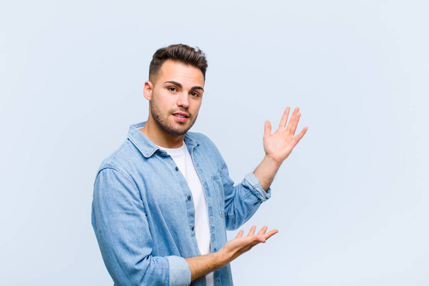 young hispanic man smiling proudly and confidently, feeling happy and satisfied and showing a concept on copy space against blue wall - Foto, Imagem