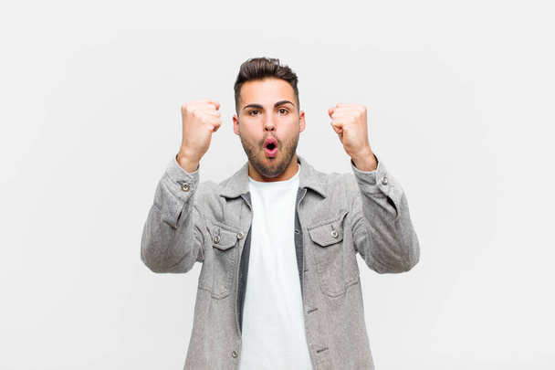 young hispanic man celebrating an unbelievable success like a winner, looking excited and happy saying take that! against gray background - 写真・画像