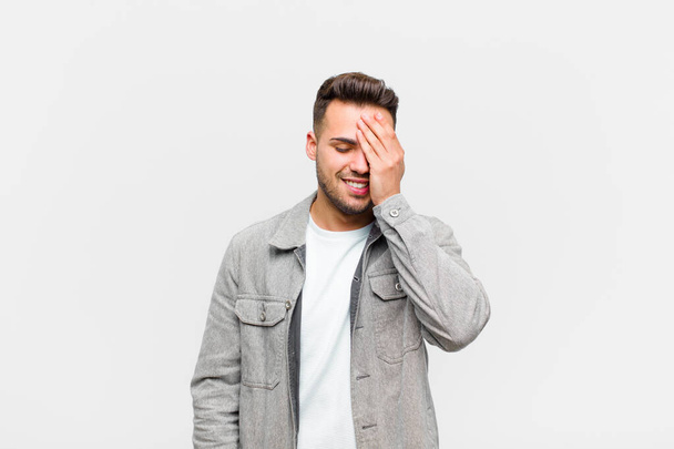 young hispanic man laughing and slapping forehead like saying doh! I forgot or that was a stupid mistake against gray background  - Фото, зображення