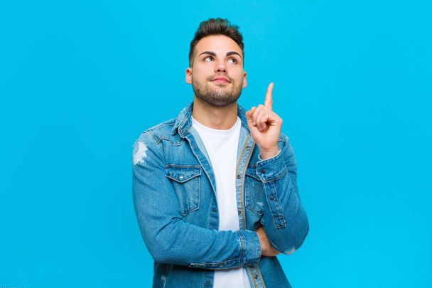 young hispanic man smiling happily and looking sideways, wondering, thinking or having an idea against blue background - Фото, зображення