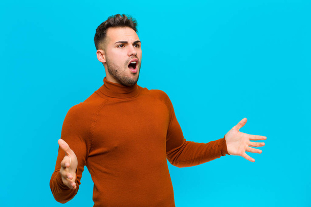 young hispanic man performing opera or singing at a concert or show, feeling romantic, artistic and passionate against blue background - Photo, Image