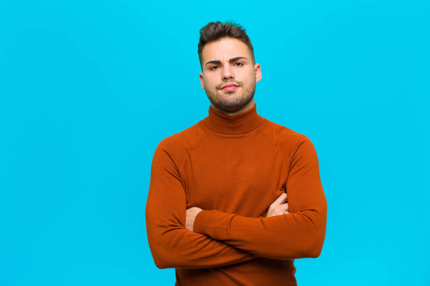 young hispanic man feeling displeased and disappointed, looking serious, annoyed and angry with crossed arms against blue background - Fotografie, Obrázek