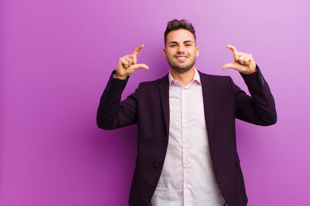 young hispanic man framing or outlining own smile with both hands, looking positive and happy, wellness concept - 写真・画像