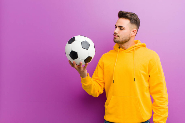 young hispanic man with a soccer ball against purple background - Foto, Imagem