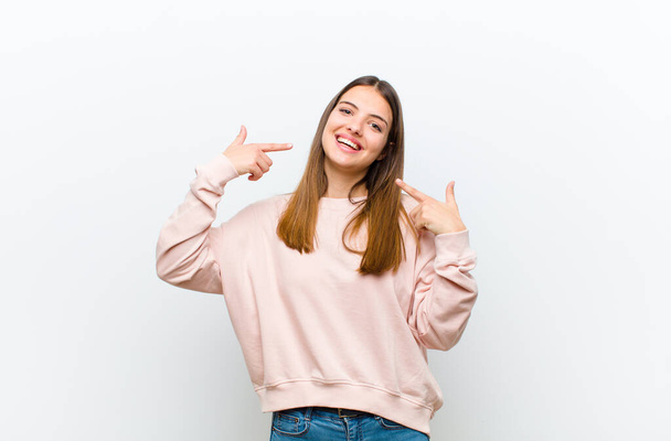 young pretty woman smiling confidently pointing to own broad smile, positive, relaxed, satisfied attitude against white background - Fotoğraf, Görsel