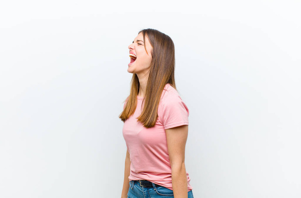 young pretty woman screaming furiously, shouting aggressively, looking stressed and angry against white background - Fotoğraf, Görsel