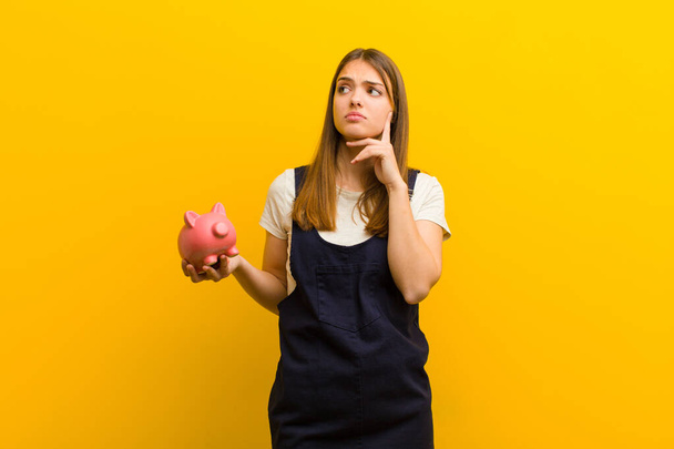 young pretty woman with a piggy bank  against orange background - Fotó, kép