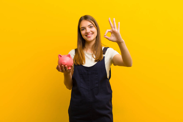 young pretty woman with a piggy bank  against orange background - Foto, Bild