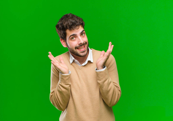 young businessman feeling shocked and excited, laughing, amazed and happy because of an unexpected surprise against green background - Foto, afbeelding