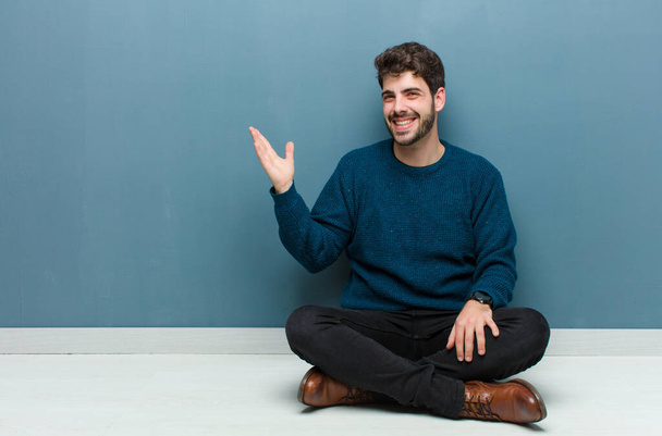 young handsome man sitting on floor feeling happy, surprised and cheerful, smiling with positive attitude, realizing a solution or idea - Foto, imagen