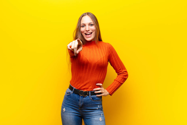 young pretty woman pointing at camera with a satisfied, confident, friendly smile, choosing you against orange background - Фото, изображение