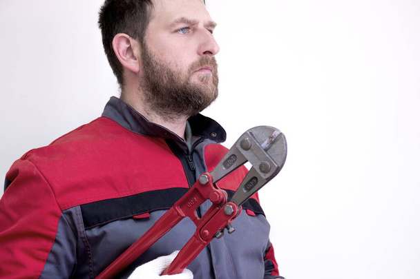 Tulum giymiş sakallı bir adam metal çubukları ısırmak için bir alet tutuyor. Uzağa bakıyor. - Fotoğraf, Görsel
