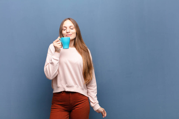 young pretty woman with a coffee against blue wall with a copy space - Foto, afbeelding