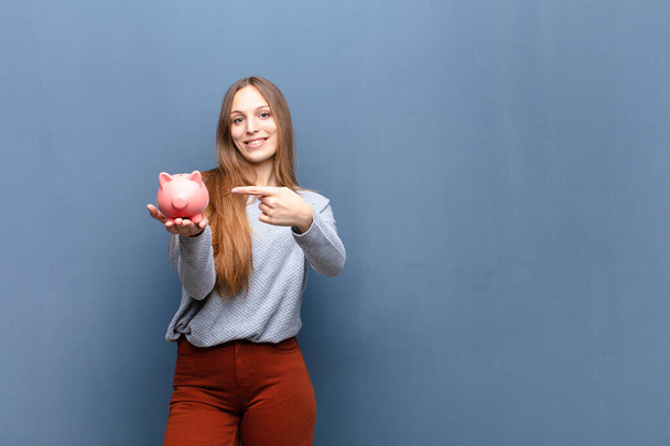 young pretty woman with a piggy bank against blue wall with a copy space - Foto, Bild