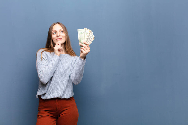 young pretty woman with dollar banknotes against blue wall with a copy space - 写真・画像