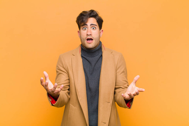 young handsome man open-mouthed and amazed, shocked and astonished with an unbelievable surprise against orange background - Foto, Imagem
