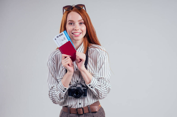 redhead happy businesswoman tourist photographer wearing sunglasses white background studio holding passport with tickets visa and camera. - Foto, imagen
