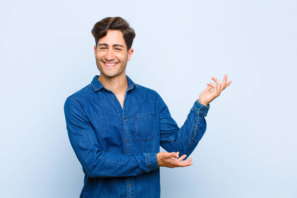 young handsome man smiling proudly and confidently, feeling happy and satisfied and showing a concept on copy space against blue background - Foto, Bild