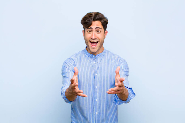 young handsome man feeling happy, astonished, lucky and surprised, like saying omg seriously? Unbelievable against blue background - Foto, Imagen