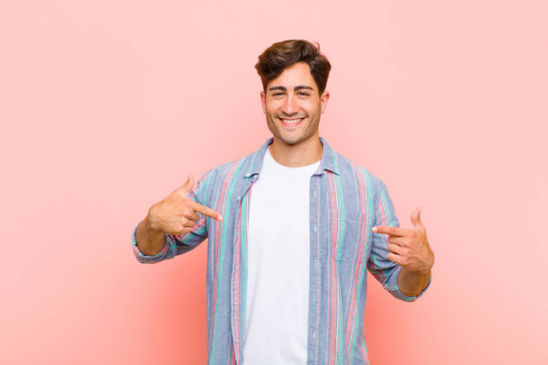 young handsome man looking proud, arrogant, happy, surprised and satisfied, pointing to self, feeling like a winner against pink background - Foto, Bild