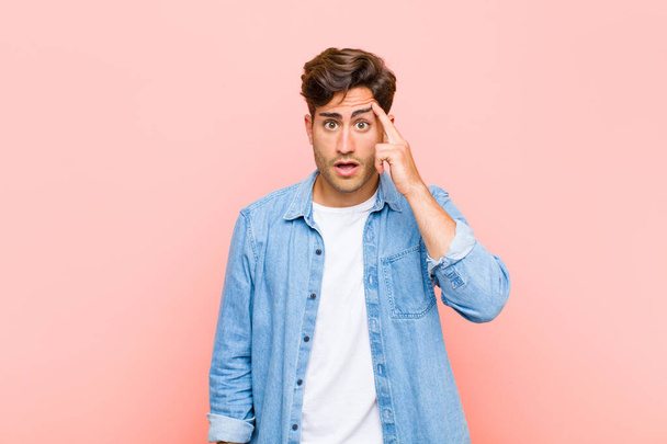 young handsome man looking surprised, open-mouthed, shocked, realizing a new thought, idea or concept against pink background - Фото, изображение