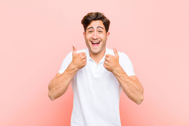 young handsome man smiling broadly looking happy, positive, confident and successful, with both thumbs up against pink background - Photo, Image