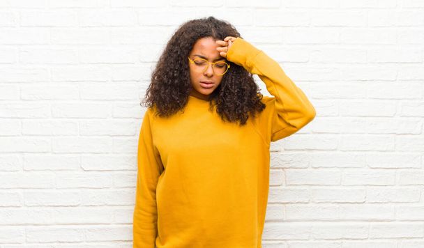 young black woman looking stressed, tired and frustrated, drying sweat off forehead, feeling hopeless and exhausted against brick wall - Foto, Bild