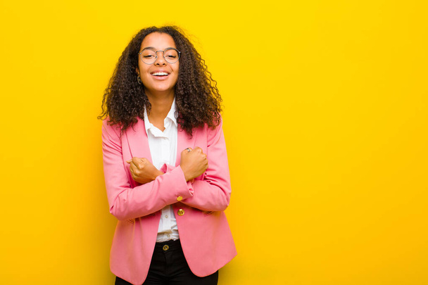 black business woman smiling cheerfully and celebrating, with fists clenched and arms crossed, feeling happy and positive against orange wall - Фото, зображення