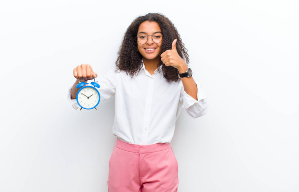 young pretty black woman with an alarm clock against white wall - Фото, изображение