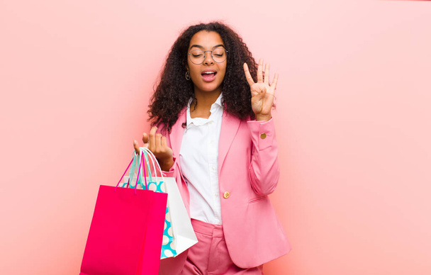 young black pretty woman with shopping bags against pink wall background - Foto, immagini