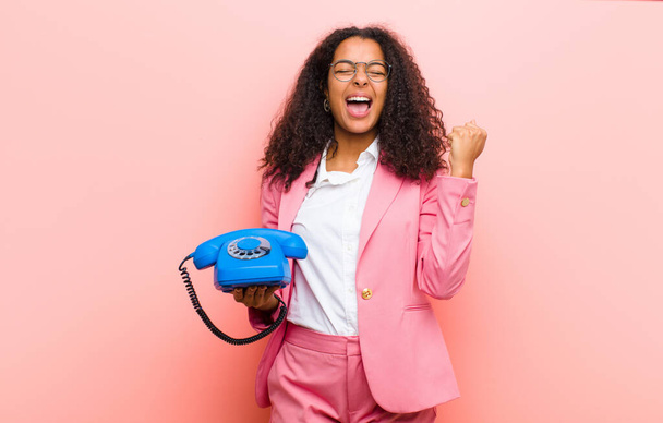 young black pretty woman with a vintage telephone against pink wall background - Foto, Imagen