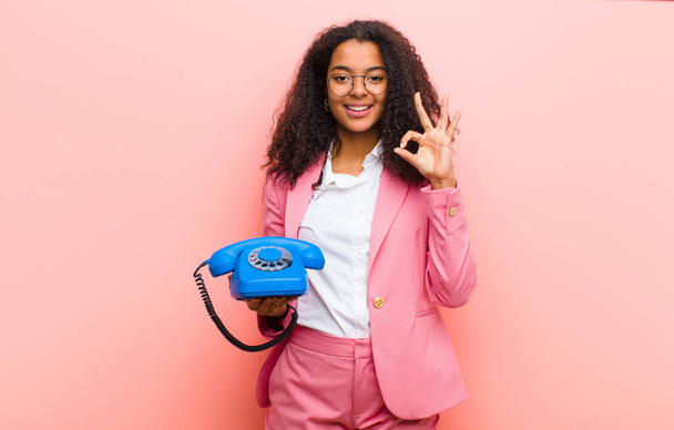 young black pretty woman with a vintage telephone against pink wall background - Zdjęcie, obraz