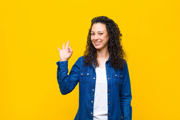 young pretty woman feeling happy, relaxed and satisfied, showing approval with okay gesture, smiling against orange wall - Фото, зображення