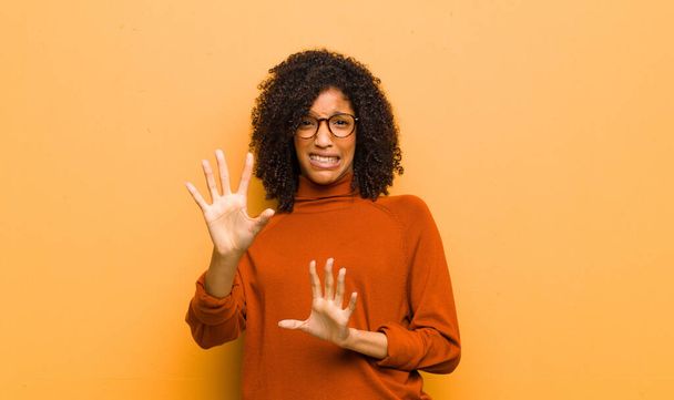 young pretty black woman feeling terrified, backing off and screaming in horror and panic, reacting to a nightmare against orange wall - Foto, imagen