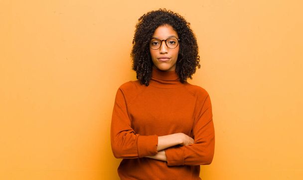 young pretty black woman feeling displeased and disappointed, looking serious, annoyed and angry with crossed arms against orange wall - Foto, Imagem