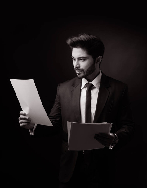 Intialainen parrakas mies liikemies, jolla on tai lukee asiakirjoja tai paperirulla seisoessaan eristyksissä valkoisella taustalla
 - Valokuva, kuva