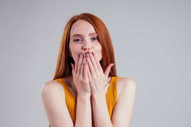 beautiful ginger hair woman with perfect skin wearing yellow shirt, looking at camera sending hands air kiss white studio background. - Foto, immagini