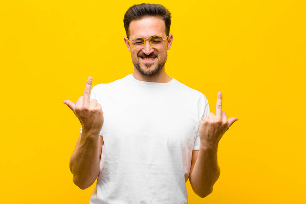 young handsome man feeling provocative, aggressive and obscene, flipping the middle finger, with a rebellious attitude against orange wall - Foto, Bild