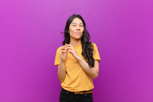 young pretty latin woman feeling proud, mischievous and arrogant while scheming an evil plan or thinking of a trick against purple wall - Fotoğraf, Görsel