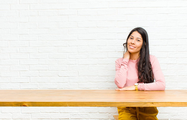 young  pretty latin woman laughing cheerfully and confidently with a casual, happy, friendly smile sitting in front of a table - Foto, afbeelding