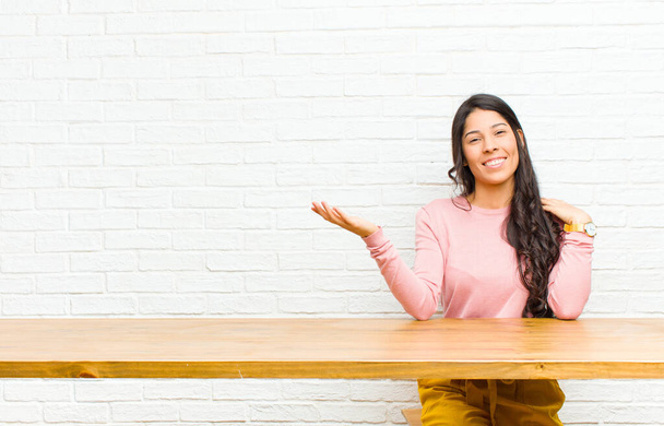 young  pretty latin woman feeling happy, surprised and cheerful, smiling with positive attitude, realizing a solution or idea sitting in front of a table - Foto, Imagen