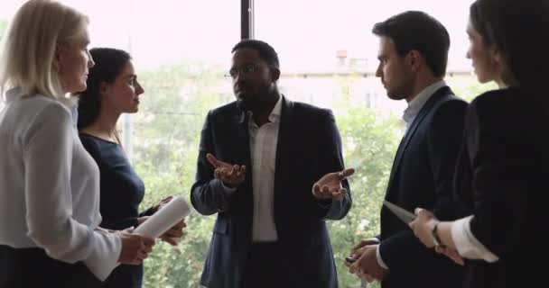 Afrykański trener biznesu komunikuje się z ludźmi biznesu stojącymi na stanowisku - Materiał filmowy, wideo