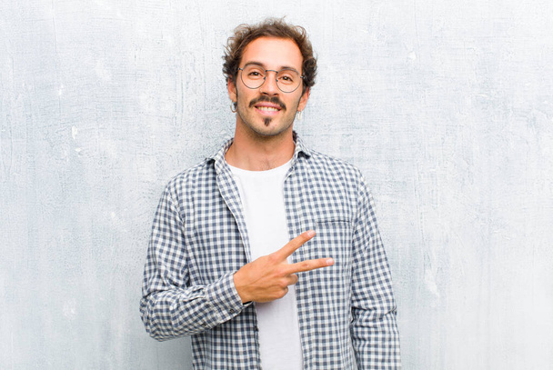young handsome man feeling happy, positive and successful, with hand making v shape over chest, showing victory or peace isolated against flat wall - Fotoğraf, Görsel