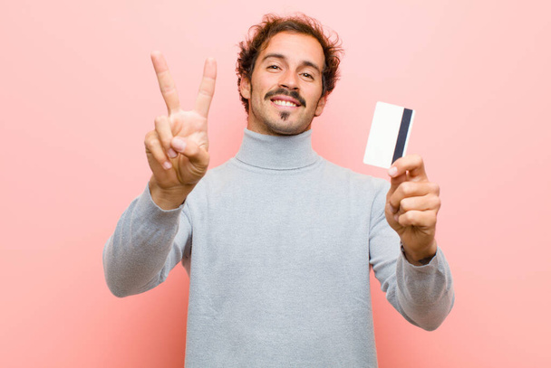 young handsome man with a credit card against pink flat wall - Foto, Bild