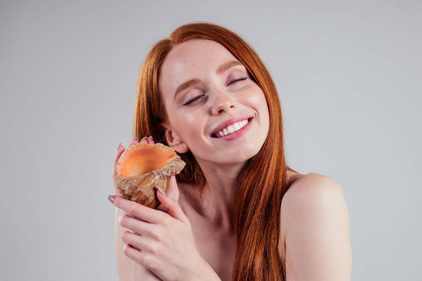 ginger redhead youth woman with snow-white dental smile listen sound from shell white background studio. - Foto, Imagem
