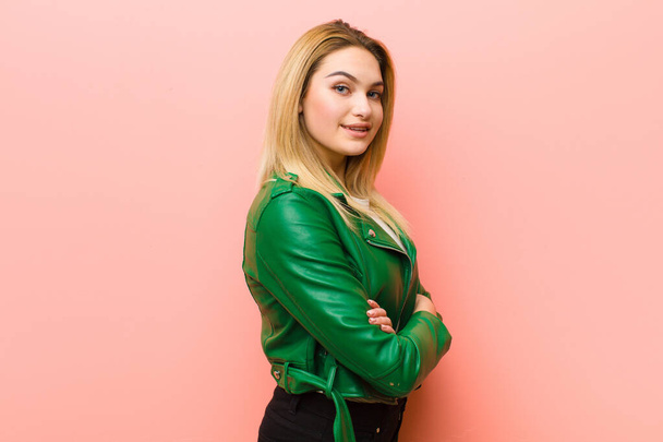 young pretty blonde woman smiling to camera with crossed arms and a happy, confident, satisfied expression, lateral view against pink flat wall - Photo, image