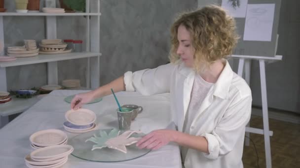 potter work, creative painter female working with newly finished pottery plate and drawing via brush at workroom - Video, Çekim