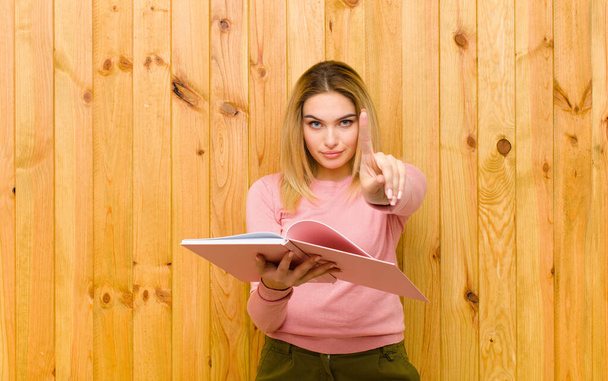 young pretty blonde woman with books against wood wall - Foto, Bild